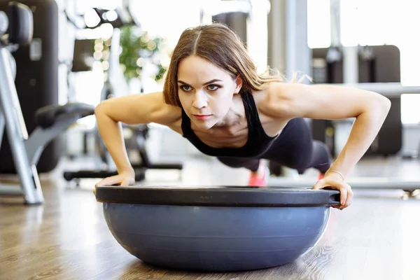 Jeune belle femme mince faire des pompes avec boule bosu dans la salle de gym — Photo