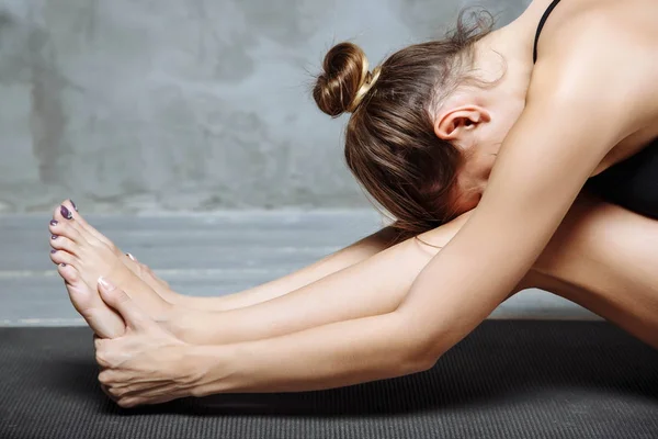 Mujer joven practicando yoga, sentada en ejercicio de flexión hacia adelante sentada, pose de paschimottanasana, haciendo ejercicio, usando ropa deportiva, interior, fondo interior casero, primer plano —  Fotos de Stock