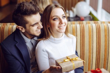 Güzel genç bir çift bir kafede kutluyor. Yakışıklı adam kız arkadaşı bir hediye kutusu veriyor