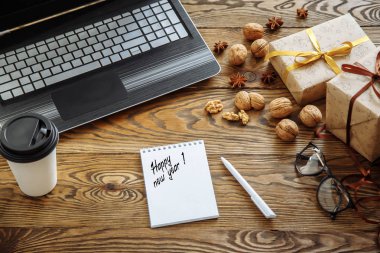 Çalışma alanı. Hediye kutuları, dizüstü bilgisayar, kahve ve ahşap masa üstünde defter.