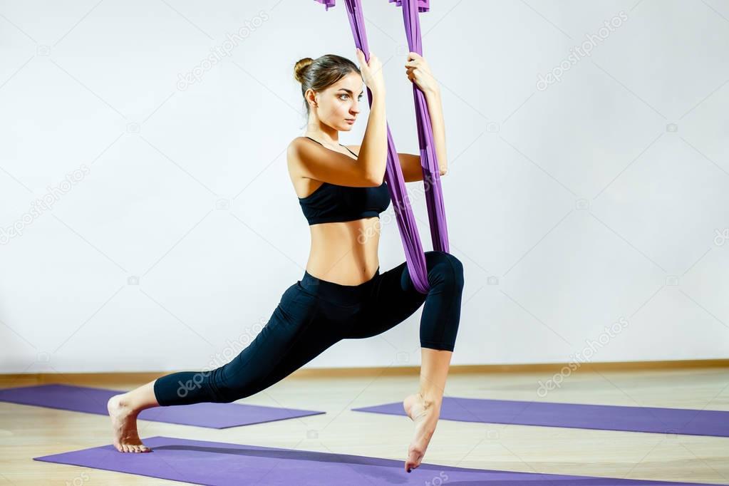 Young woman doing aerial yoga exercise or antigravity yoga indoor. Flying, fitness, stretch, balance, exercise and healthy lifestyle people.