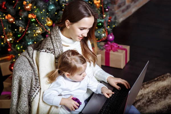 Mother showing baby something in laptop near Christmas tree — Stock Photo, Image