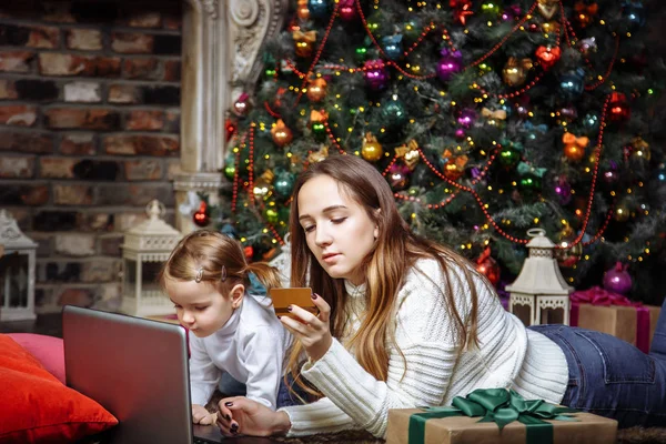 A young mother with a daughter buy gifts using laptop and credit card. The concept of preparing for Christmas and new year. — Stock Photo, Image