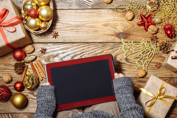 Tablet bilgisayarda ahşap arka plan küçük bir çocuğun elleri. Yılbaşı süsleri ve hediyeleri. Kopya alanı.