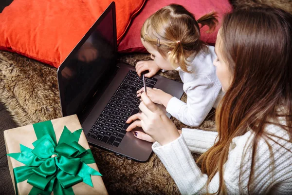 A young mother with a daughter buy gifts using laptop and credit card. The concept of preparing for Christmas and new year. — Stock Photo, Image