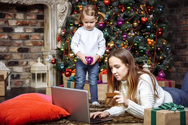 A young mother with a daughter buy gifts using laptop and credit card. The concept of preparing for Christmas and new year. — Stock Photo, Image