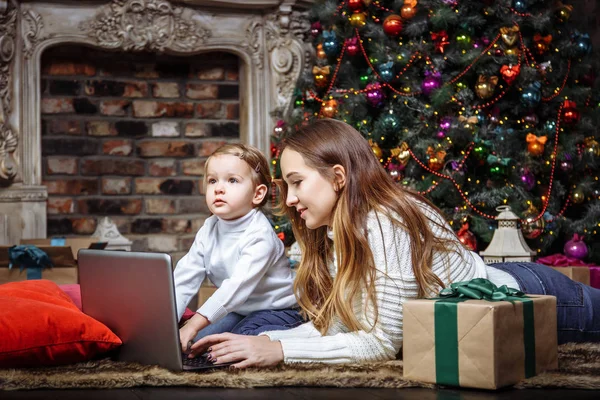 Happy young family mother and daughter using a laptop while sitting near the Christmas tree — Stock Photo, Image