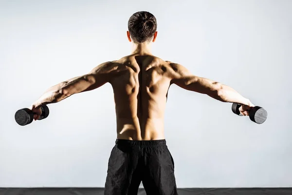 Вид со спины. Мускулистый человек делает упражнения с гантелями . — стоковое фото