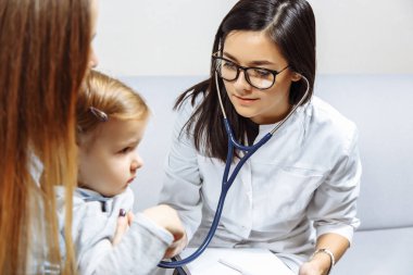 Küçük kız stetoskop ile inceleyerek kadın çocuk doktoru. Çocuğunu tutan anne