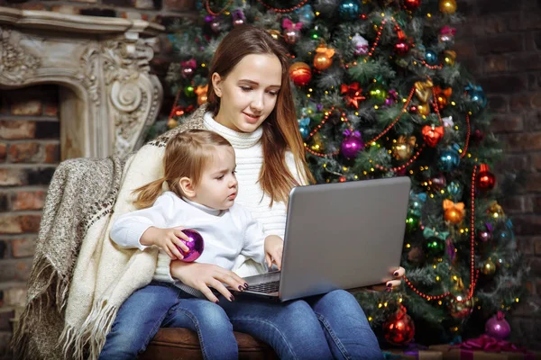 Happy young family mother and daughter using a laptop while sitting near the Christmas tree — Stock Photo, Image