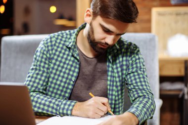 Kafeterya masada oturan ve Not Defteri'nde, yaratıcı fikirler aşağı yazma kendine güvenen genç Yöneticisi bulanık arka plan