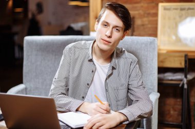 Üniversite Kampüsü, dizüstü bilgisayarda çalışarak, kafede otururken iş planı yazma hipster işadamı dersler hazırlamak genç erkek öğrenci bilgilerini bir defterde yazar..