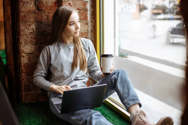 Красивая молодая женщина сидит на подоконнике и использует ноутбук — стоковое фото
