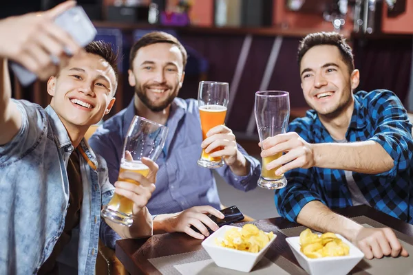 De beaux amis boivent de la bière, font du selfie et sourient tout en se reposant dans un pub . — Photo