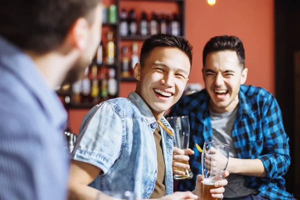 A companhia de jovens bonitos se divertindo juntos. Amigos rindo e bebendo cerveja no bar — Fotografia de Stock