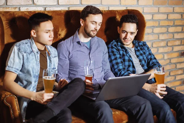 Drei gut gelaunte junge Männer, die das Spiel am Laptop verfolgen und ihr Team in der Bar unterstützen. — Stockfoto