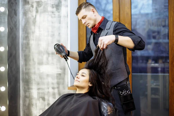 Hairdresser dries hair with a hairdryer in beauty salon.