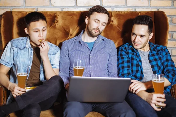 Drei gut gelaunte junge Männer, die das Spiel am Laptop verfolgen und ihr Team in der Bar unterstützen. — Stockfoto