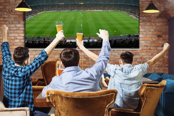 Grupo de jovens torcendo em seu time de futebol favorito assistindo o jogo na TV no pub local tomando cerveja . — Fotografia de Stock