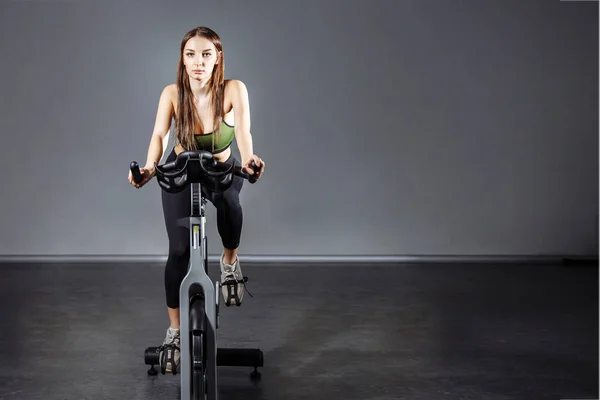 Mujer joven haciendo ejercicio en la bicicleta estática en el gimnasio . — Foto de Stock