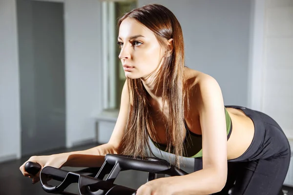 Mujer joven haciendo ejercicio en la bicicleta estática en el gimnasio, entrenamiento cardio intenso . — Foto de Stock