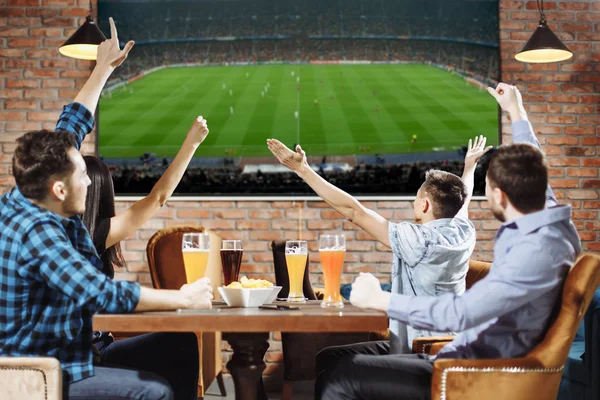 Victory! Group of young beautiful friends watching TV and cheering for their team while resting in pub — Stock Photo, Image