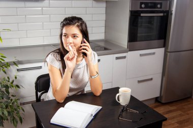 Genç kadın mutfakta otururken telefon üzerinden yemek siparişi