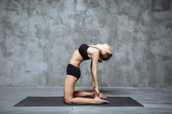 Mujer atractiva joven practicando yoga, estirándose en ejercicio de Ustrasana, pose de camello, interior del hogar o fondo del club deportivo — Foto de Stock