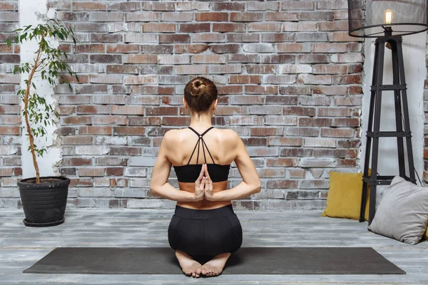 Jovem praticando ioga com namaste atrás das costas, sentado em exercício de seiza, pose de vajrasana, casa interior fundo — Fotografia de Stock