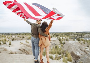 Doğada Amerikan bayrağı sallayan mutlu genç bir çift. Bağımsızlık Günü, yaşam tarzı, seyahat kavramı