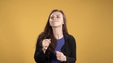 Mutlu genç kadın parmaklarını şaklatıyor ve sarı arka planda dans ediyor.