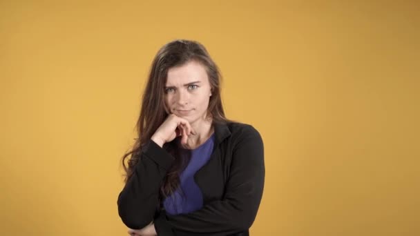 Молодая женщина недоверчиво смотрит в камеру на желтом фоне — стоковое видео
