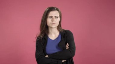 Kolları pembe arka planda çapraz duran düşünceli genç bir kadın.