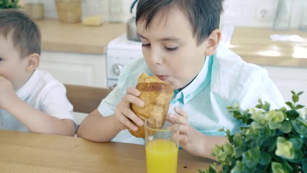 二人の子供が台所でクロワッサンを食べる — ストック動画