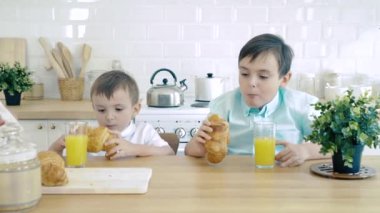 Kahvaltıda mutlu bir aile. İki erkek bebek mutfakta kruvasan yiyor.