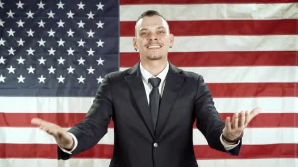 身穿西装的年轻人在美国国旗的衬托下做手势和讲话 — 图库视频影像