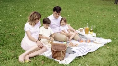 Mutlu bir aile ve çocuklar piknik sırasında çimlerin üzerinde dinleniyorlar..