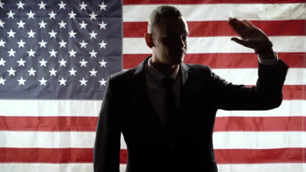 Egy üzletember sziluettje, aki az amerikai zászló hátterében üdvözli a közönséget. — Stock videók