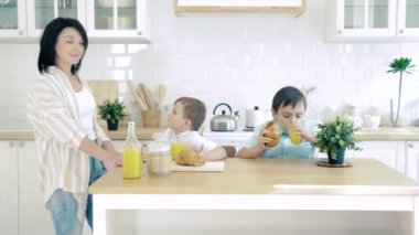 Kahvaltıda mutlu bir aile. İki erkek bebek mutfakta kruvasan yiyor.
