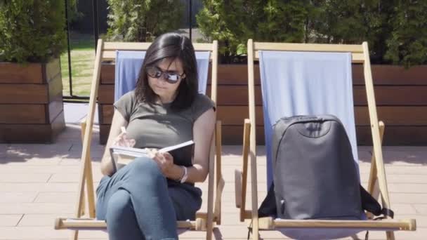 Jeune Femme Lunettes Soleil Prenant Des Notes Dans Carnet Extérieur — Video