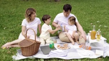 Mutlu bir aile ve çocuklar piknik sırasında çimlerin üzerinde dinleniyorlar..