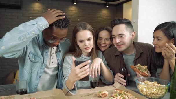 スマートフォンを見て笑いながら バーや自宅でピザや軽食を食べている多民族グループ — ストック動画