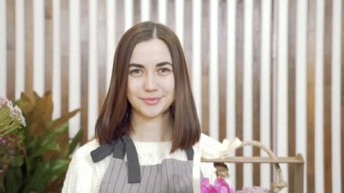 Çiçekçide ya da atölyede kameraya gülümseyen önlüklü sevimli kadın çiçekçinin yavaş çekim portresi. İnsanlar, iş ve çiçekçilik kavramı