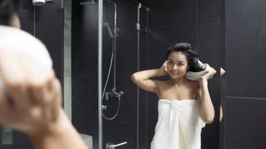 Genç bir kadın banyo yaptıktan sonra havluyu kafasından çıkarıyor ve saçlarını kurutuyor..
