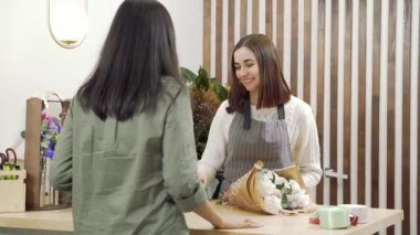 Genç bir çiçekçi bir bayan müşteriyle buluşup gülümsüyor ve bir mağazada ya da atölyede ona bir buket çiçek veriyor. İnsanlar, alışveriş, satış, çiçekçilik ve tüketim kavramı