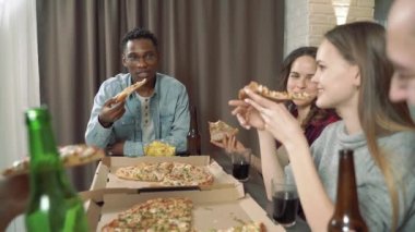 Mutlu çok ırklı arkadaşlar bira içiyor, pizza yiyor ve evdeki oturma odasında komik bir şakaya gülüyorlar..