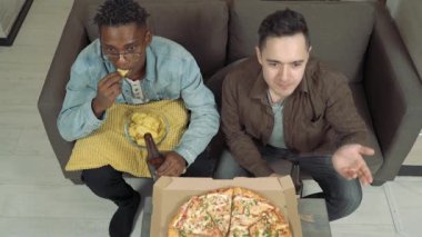Televizyonda maç izleyen iki arkadaş. Çocuklar evde kanepede otururken bira içip, pizza yiyip atıştırıyorlar.