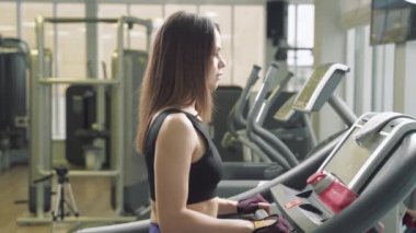 Vücut geliştiren kadın spor salonunda koşu bandında yürüyor. Spor salonunda koşu makinesi kullanan atletik bir kız.