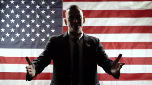 Silhouette of a man in a suit gesticulating and speaking against the background of the American flag.