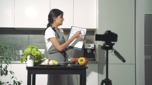 Mujer joven nutricionista hablando sobre el índice glucémico y el contenido calórico de los alimentos y la grabación de un video en la cámara digital en la cocina en casa. Vlogging y concepto de redes sociales . — Vídeos de Stock